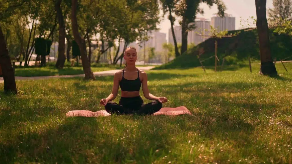 a woman sitting in a yoga pose on a mat in the grass